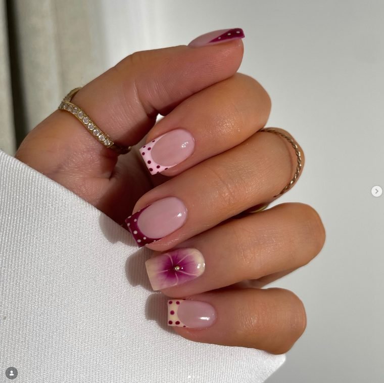 Short square nails with berry and pink polka dot French tips and a blooming purple flower accent
