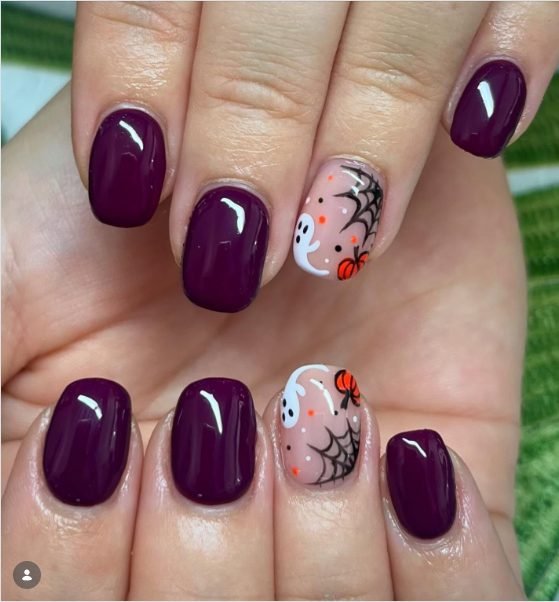 Short glossy deep plum nails with a nude accent nail featuring a ghost, spider web and pumpkin