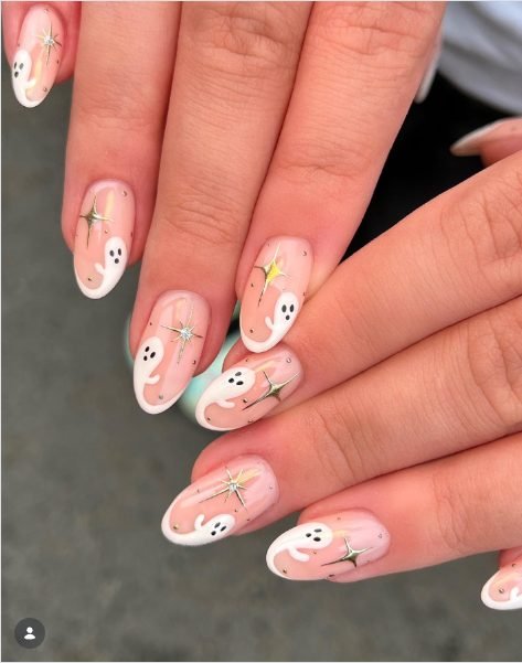 Sheer pink almond nails with white ghosts peeking from the tips and gold chrome sparkle stars