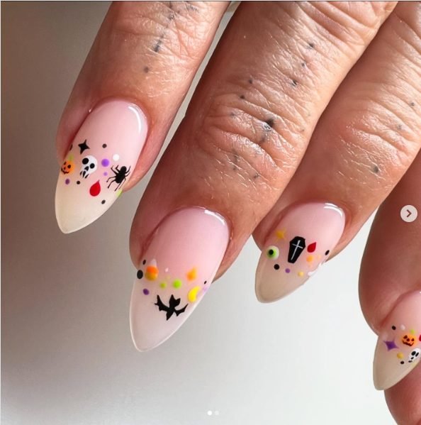 Sheer pink nails with tiny skulls, pumpkins, bats, spiders and colorful dots near the tips
