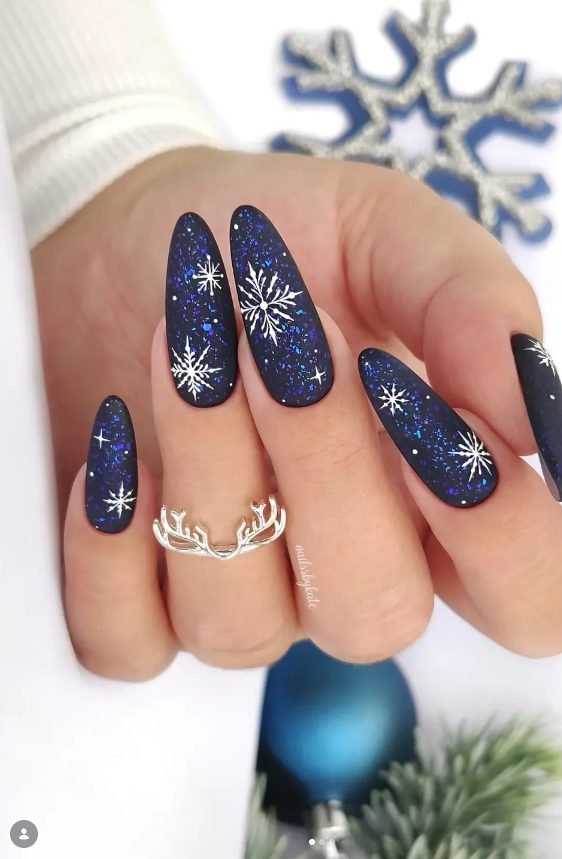 Long almond matte midnight blue nails with blue glitter flakes and white snowflakes