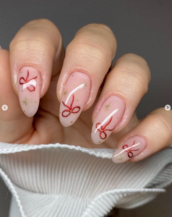 Sheer pink almond nails with hand-painted red ribbon bows and small gold stars