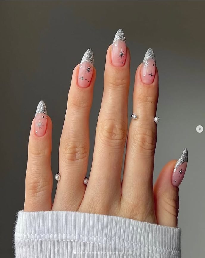 Long almond sheer pink nails with silver glitter French tips, silver starburst stars and small studs