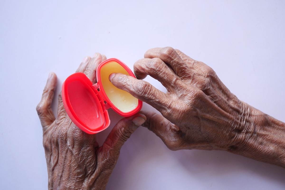 Close-up of senior hands applying hand cream from a red container